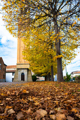 Fototapeta premium Tall brick tower surrounded by vibrant autumn trees and fallen leaves in a quaint town