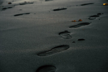 A black volcanic sand on a beach closeup with a person footprints.