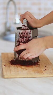 A woman grates red beet in the kitchen