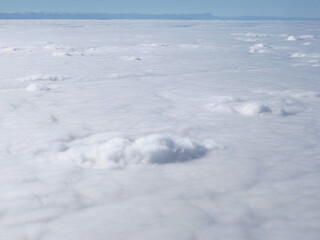 A tranquil aerial view above a vast sea of clouds with a distant mountain horizon under a clear blue sky. Soft, fluffy formations convey calm, freedom, and dreamlike atmosphere.