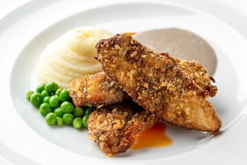 Golden brown crispy chicken goujons served with a side of creamy mashed potatoes, bright green peas, and a savory gravy on a clean white plate