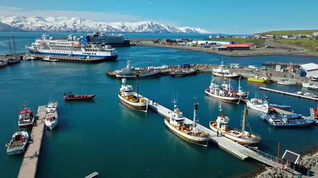 Aerial view of Husavik port filled with fishing and whale-watching boats. Calm waters reflect the bright Icelandic summer sky.