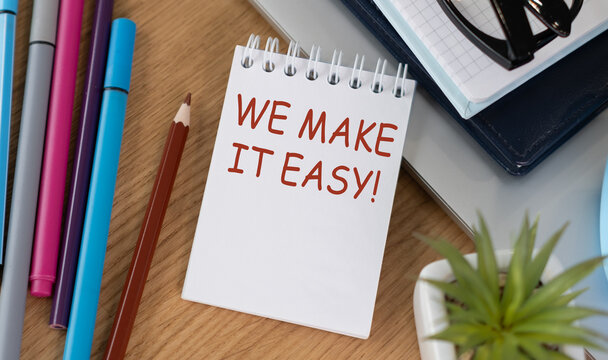 A notebook with the words We Make it Easy written on it. The notebook is on a desk with a pencil, pens, and a laptop