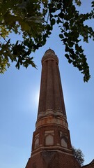 Fototapeta premium Iconic fluted Yivli Minaret in Kaleici against a bright blue sky, with sun flare and framing green leaves
