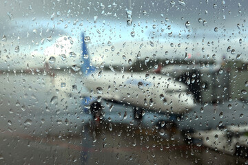 Blurred view to air field with aircraft through the glass with rain drops in the overcast weather in the evening
