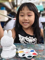 cute little thai Girl Painting a Ceramic Figurine at Table