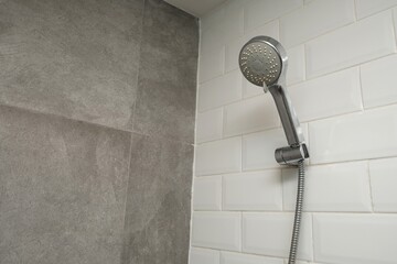 Close-up of a handheld shower head attached to a tiled bathroom wall, featuring a mix of white and gray tiles in a clean design.  © Ahmad