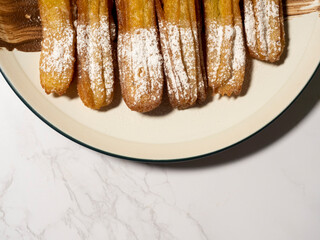 Spanish Churros with Sugar and Chocolate Dip. Crispy fried dough sticks coated with powdered sugar and served with rich chocolate dipping sauce on a clean white plate. Sweet snack presentation.