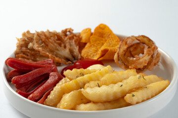 Tasty assorted fried snacks on a white plate, including crunchy onion rings, french fries, tortilla chips, fried mushrooms, and sausage bites with ketchup and mayonnaise dip.