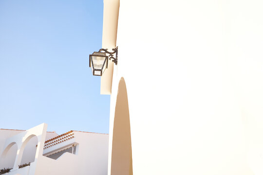 Fototapeta Low angle view of traditional forged street lamp on beige house wall, cloudless blue sky and part of adjoining building seen on background