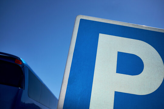 Parking traffic sign and modern blue tourist coach against sunny cloudless sky, close-up shot