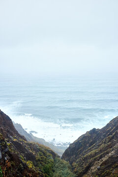 Picturesque view from mountains: stormy Atlantic Ocean with high waves on its surface, grey foggy sky, nothing seen on horizon