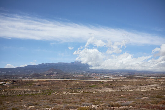 Panoramic view of Spanish coastal town and high mountains in distance, sunny blue sky hovering over them, big field on foreground