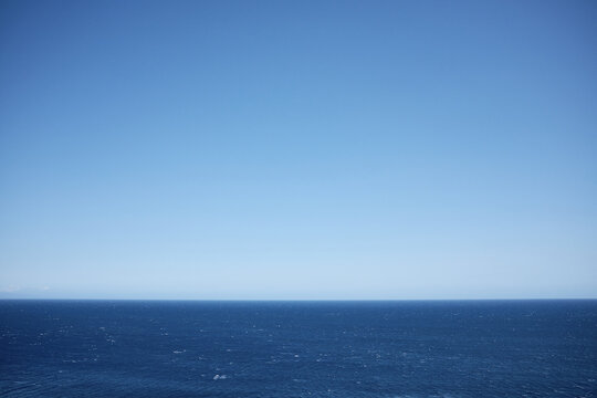 Cloudless blue sky hovering over endless surface of sea with small waves