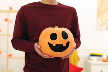 Halloween celebration. Man holding pumpkin with drawn spooky face indoors, closeup