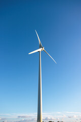 Drone aerial view of a wind farm over countryside roads and fields beneath a vivid blue sky. Renewable power, technology, and grid concept; no people.