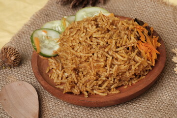 Traditional Indonesian-Middle Eastern fusion dish Nasi Kebuli, served with sliced cucumber and carrots on a rustic wooden plate over burlap.