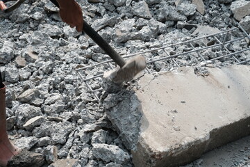 Person using a sledgehammer to break concrete surrounded by rubble and metal rebar, illustrating manual labor in demolition work.
