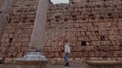 A woman holding a camera walks past ancient stone walls and columns. The contrast between heritage and digital creativity captures a timeless exploration mood.