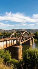 Rustic railway bridge stretching over a tranquil river on a sunny day