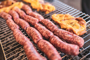 Raw sausages and meat grilling over charcoal barbecue