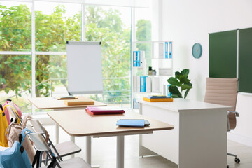 Stylish furniture, chalkboard and flip chart in classroom