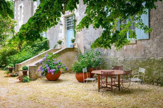 Charming Outdoor Courtyard With Round Table, Metal Chairs, and Purple Hydrangeas by Old Stone House