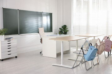 Green chalkboard, backpacks and stylish furniture in classroom. Mockup for design