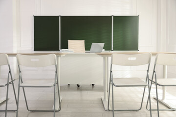 Green chalkboard and stylish furniture in classroom. Mockup for design