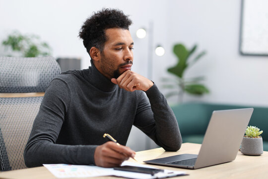 Man working with laptop and writing at table in office
