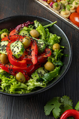 Fresh colorful vegan salad with green leaves and red bell pepper served in black plate on dark wooden table, healthy vegetarian meal for detox diet and clean eating close-up