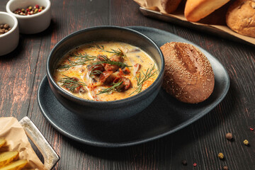 Creamy mushroom soup with herbs and bread roll on dark wooden table, rustic restaurant serving, hot homemade soup in ceramic bowl, cozy lunch or dinner concept, traditional comfort food