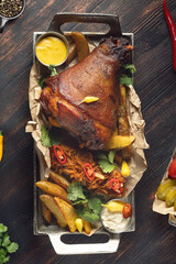 Roasted pork knuckle with sauerkraut, baked potatoes and mustard sauce, traditional German or Czech cuisine dish on rustic wooden table, restaurant serving, hearty meat dinner concept