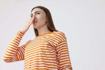 Young woman suffering from bad smell and covering her nose indoors, low angle view. Space for text