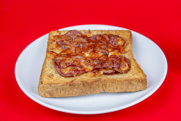 Toasted bread with pepperoni or salami and melted cheese on a white plate, red background.