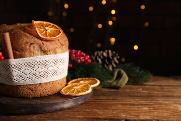 Christmas food. Delicious Panettone cake, ingredients and festive decor on wooden table against background with blurred lights, space for text. Bokeh effect