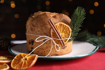 Christmas food. Delicious Panettone cake, spices and festive decor on table against background with blurred lights, closeup. Bokeh effect