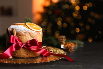 Christmas food. Delicious Panettone cake, ingredients and festive decor on black table against background with blurred lights, space for text. Bokeh effect