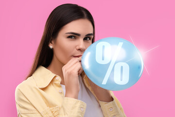 Woman blowing balloon with percent sign on pink background. Discount