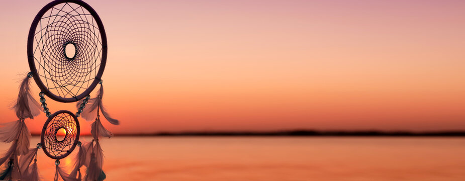 Dream catcher with feathers against sea at sunset. Banner design