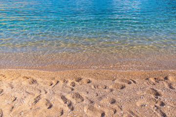 Clear turquoise water gently reaching sandy shore on a sunny beach day