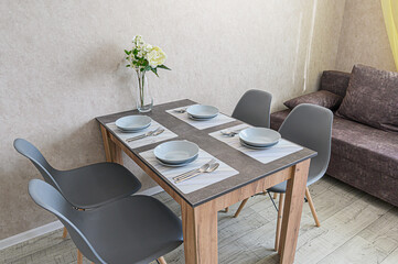 A dining room with a table set for four, featuring grey chairs and neutral decor. A bouquet of white flowers sits on the table