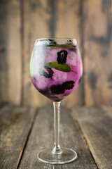 Elegant blackberry cocktail in wine glass on rustic wooden background. Selective focus.