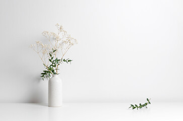 Minimalist arrangement featuring a white ceramic vase with delicate flowers and greenery on a clean surface, creating a serene and modern aesthetic with ample copy space