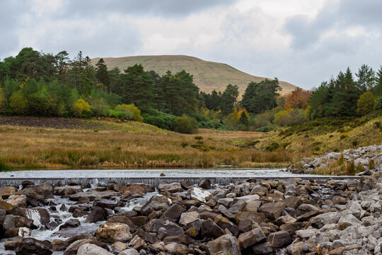 The Taf Fechan river flows over a rocky riverbed downstream from the decommissioned Upper and Lower Neuadd Reservoirs in autumn at Bannau Brycheiniog (Brecon Beacons National Park), Powys, Wales