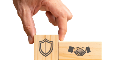Hand placing a wooden block with a shield over another with a handshake