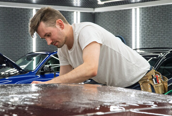 A specialist in wrapping a car with violet chameleon-colored vinyl film in the process of work. Car wrapping close-up. Car wrapping specialists cover the car with vinyl sheet or film. Selective focus.