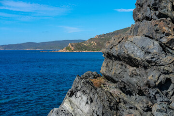 Coastal landscape with green hills and rocky shoreline by the blue sea under a sunny sky.