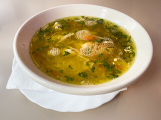 Hearty chicken soup with vegetables in white ceramic bowl on table
