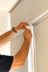 Installation of light gray roller blinds with reflective foil coating on windows.